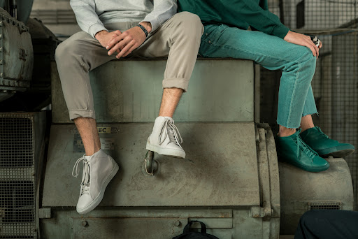 A man and a woman seat on a machine showing their sneakers